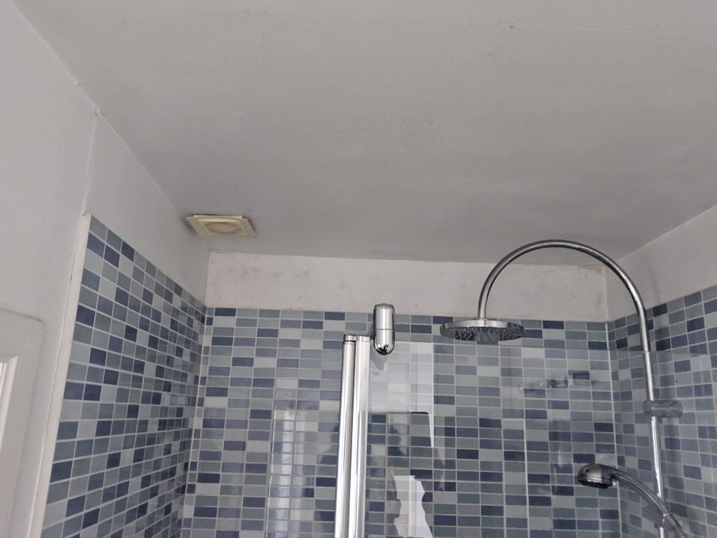 Vochtige badkamer met schimmel op plafond en onvoldoende werkende afzuiging