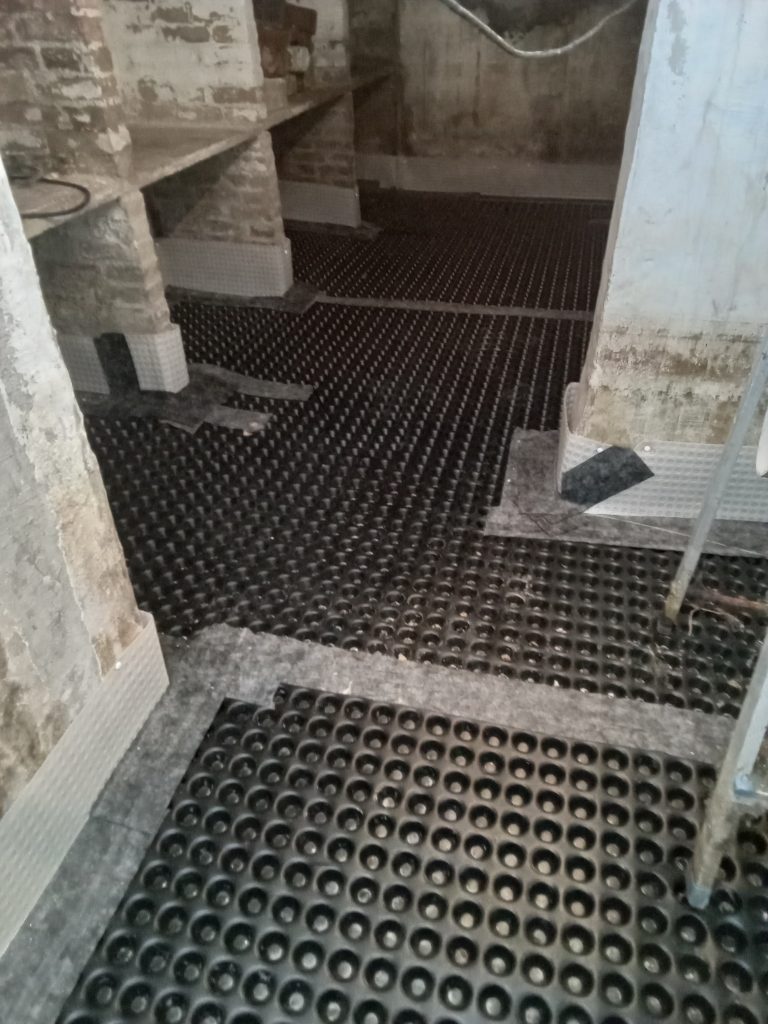 Drainagemat geplaatst op vochtige vloer in kelderruimte als structurele oplossing voor waterinfiltratie