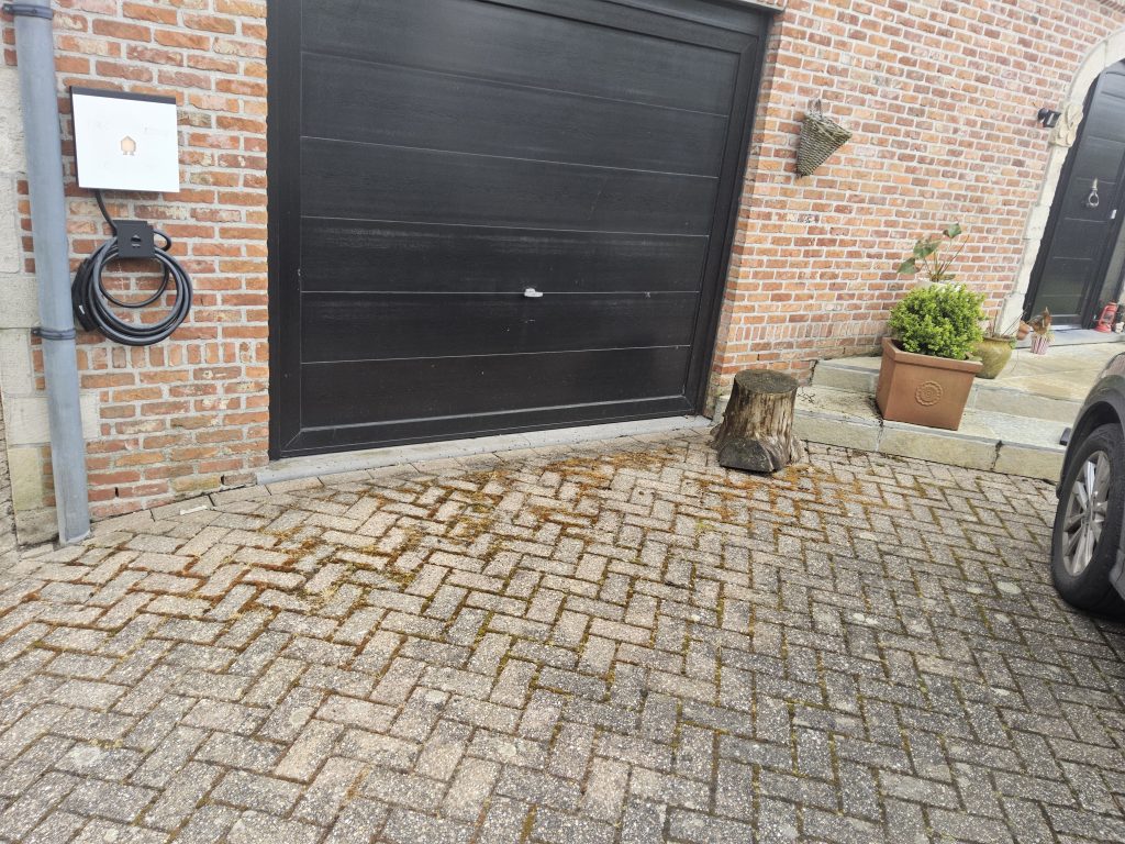 Oprit met bestrating voor een garage; vochtige vloer met mosgroei wijst op aanhoudend vocht