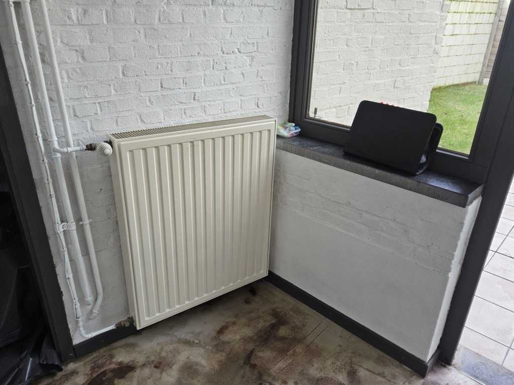 Binnenhoek met radiator onder raam; vochtige vloer met donkere vlekken rondom de plint
