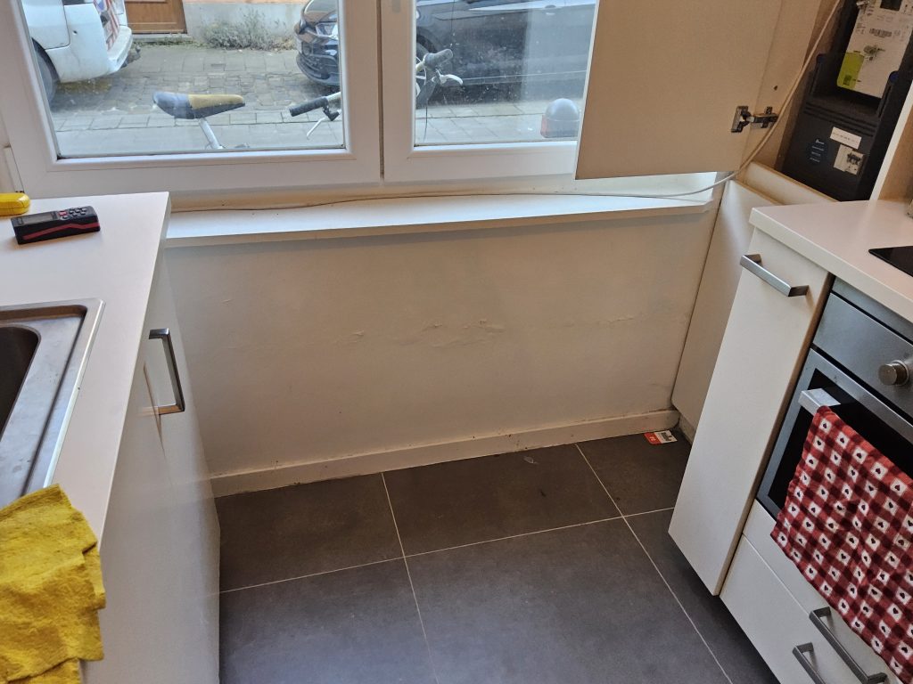 Vochtplekken en blaasvorming op de keukenmuur onder een raam door condensatievocht